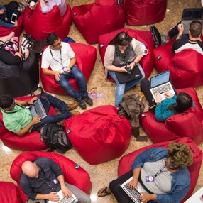 Overhead view of employees sitting in communal bean bag chairs working on laptops